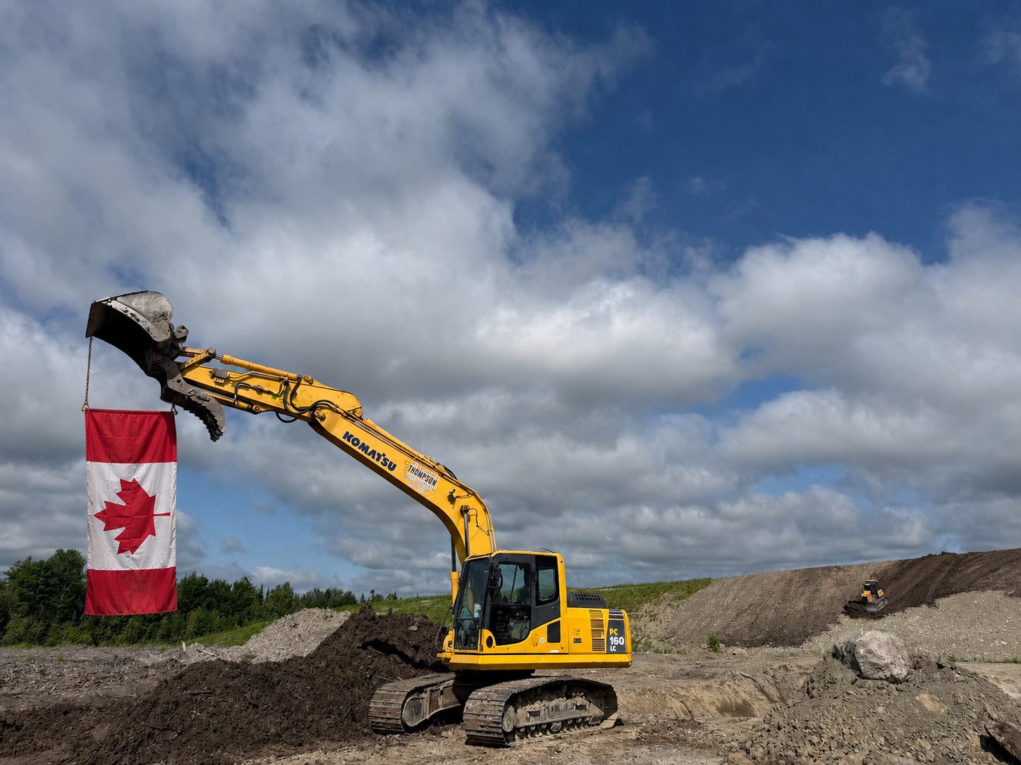 Pelle mécanique Komatsu de Transport Excavation Thompson sur un chantier, portant le drapeau canadien